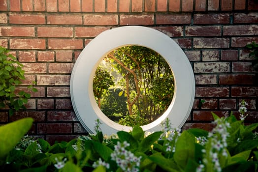 Wall brick and circle white window over green bush in the park with the sunlight. Authentic tree bush leaves wallpaper detail pattern backdrop for fence design architecture and decoration
