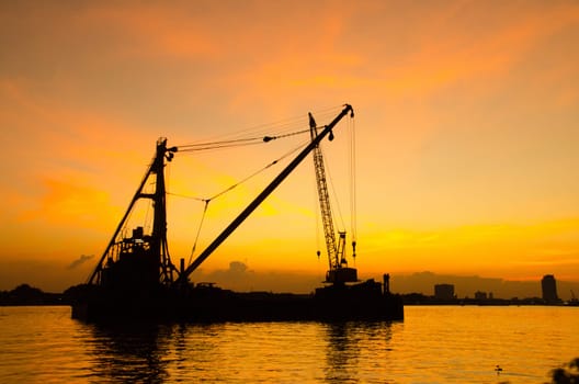 Silhouette construction site floating over river with reflection on sunset. Construction concept.