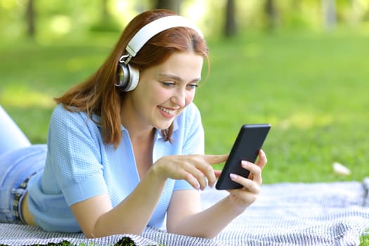 Happy woman listening to music checking phone in a park