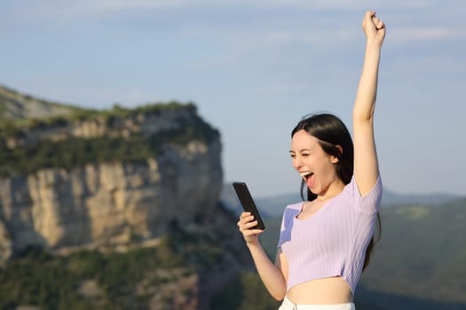 Excited asian woman checking phone in the mountain