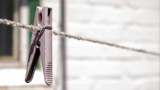 Plastic clothespins hang in a row on the rope. Rope outdoors, on a blurred background in a sunny garden. Clothesline on the street. Clothespins