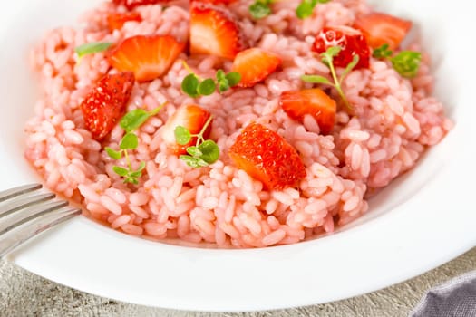 Risotto with strawberry fruits served in a white dish on a grey stone table. flat lay with copy space. Italian gourmet cuisine. Selective focus.