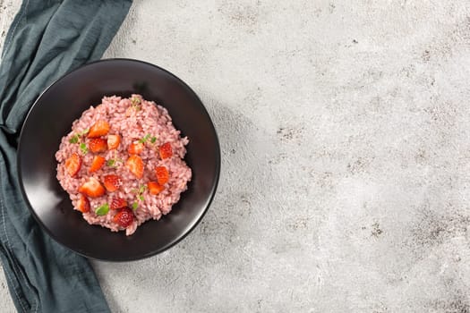 Risotto with strawberry fruits served in a black dish on a grey stone table. flat lay with copy space. Italian gourmet cuisine. Selective focus.