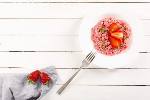 Risotto with strawberry fruits served in a white dish on a wood table. flat lay with copy space. Italian gourmet cuisine. Selective focus.