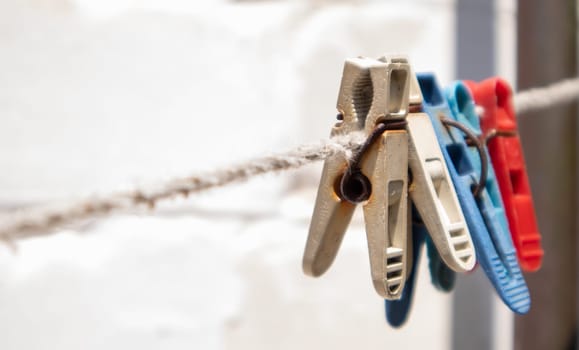 Plastic clothespins hang in a row on the rope. Rope outdoors, on a blurred background in a sunny garden. Clothesline on the street. Clothespins