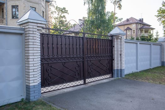 Modern private brown wrought iron large gate of the house. Home design and decoration ideas. Iron door for yard fencing. Facade of a house on a city street