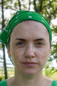 Portrait, close-up. Beautiful young woman without makeup in a green T-shirt and a green headdress from the sun on a sunny summer day outdoors. Sunlight. Vertical photography