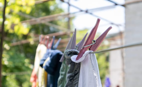 Plastic clothespins hang in a row on the rope. Rope outdoors, on a blurred background in a sunny garden. Clothesline on the street. Clothespins