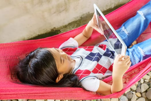 The girl lying in hammock with playing tablet pc.