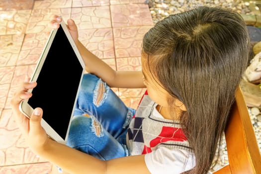 The girl sitting on wooden chair with playing tablet pc.