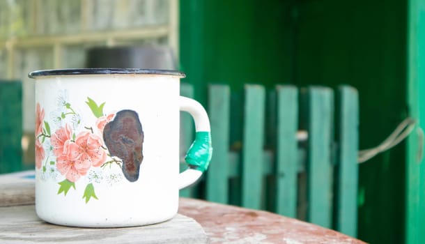 Vintage enamel mug. An old large metal mug in the village on the well. Empty dishes in the courtyard of a rural house as a traditional thing in the villages