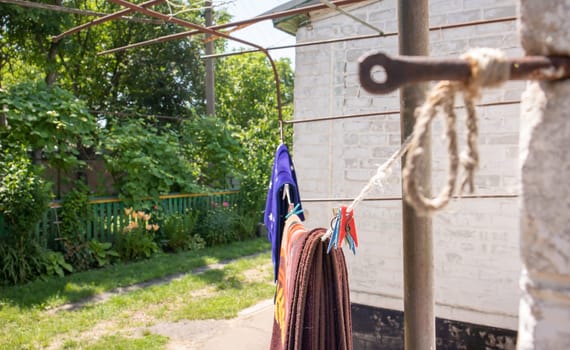Plastic clothespins hang in a row on the rope. Rope outdoors, on a blurred background in a sunny garden. Clothesline on the street. Clothespins