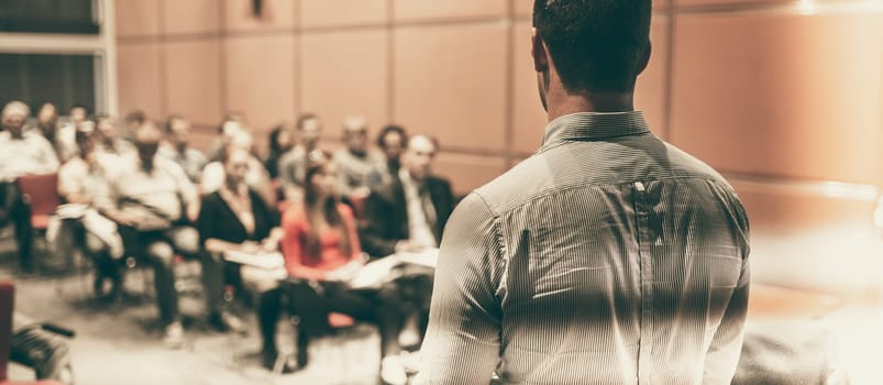 Speaker giving a talk on corporate business conference. Unrecognizable people in audience at conference hall. Business and Entrepreneurship event.