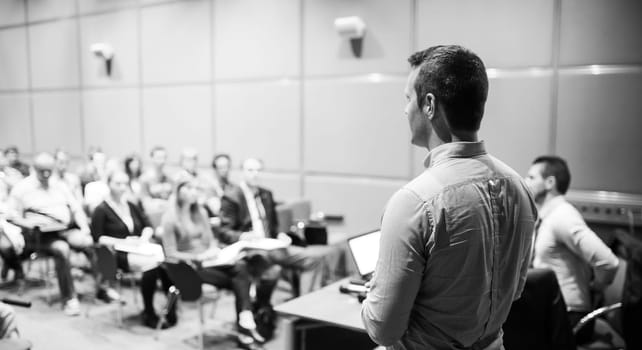 Speaker giving a talk on corporate business conference. Unrecognizable people in audience at conference hall. Business and Entrepreneurship event. Black and white.