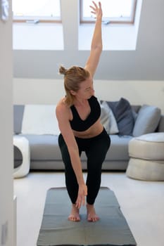 Beautiful blonde woman doing home workout indoors. Woman practice yoga at home. Fit girl using workout tutorials for healthy active lifestyle. Woman using quarantine for home workouts and stretching
