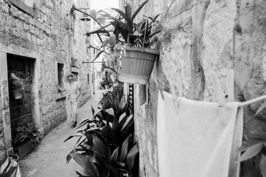 Beautiful blonde young female traveler wearing straw sun hat sightseeing and enjoying summer vacation in an old traditional costal town at Adriatic cost, Croatia. Black and white