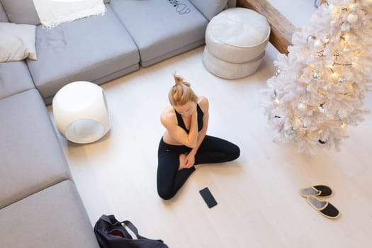 Beautiful blonde woman doing home workout indoors. Woman practice yoga at home. Fit girl using workout tutorials for healthy active lifestyle. Woman using quarantine for home workouts and stretching