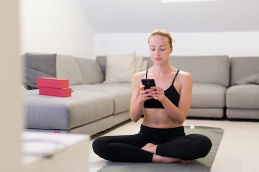 Beautiful blonde woman doing home workout indoors. Woman practice yoga at home. Fit girl using workout tutorials for healthy active lifestyle. Woman using quarantine for home workouts. Stretching