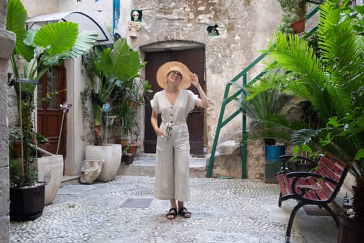Beautiful blonde young female traveler wearing straw sun hat sightseeing and enjoying summer vacation in an old traditional costal town at Adriatic cost, Croatia.