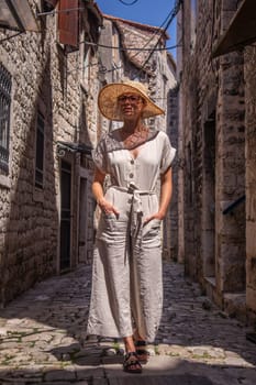 Beautiful blonde young female traveler wearing straw sun hat sightseeing and enjoying summer vacation in an old traditional costal town at Adriatic cost, Croatia.