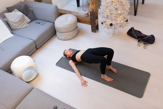 Beautiful blonde woman doing home workout indoors. Woman practice yoga at home. Fit girl using workout tutorials for healthy active lifestyle. Woman using quarantine for home workouts and stretching