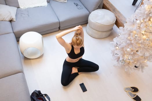 Beautiful blonde woman doing home workout indoors. Woman practice yoga at home. Fit girl using workout tutorials for healthy active lifestyle. Woman using quarantine for home workouts and stretching