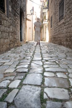 Detail shot of female legs wearing comfortable travel sandals walking on old medieval cobblestones street dring sightseeing city tour. Travel, tourism, and adventure concept.
