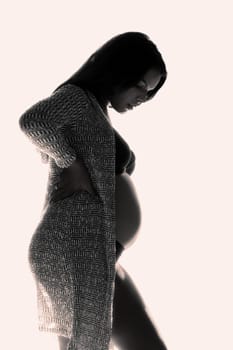 Backlit low key photo of a young pregnant woman.