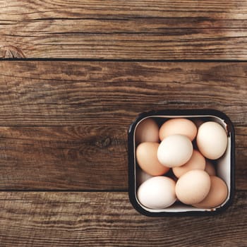 Flat lay with metal can basket full of organic chicken eggs on wooden background. Organic household concept with eggs from free-range and pasture raised hens