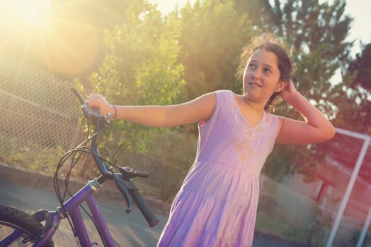 Happy young girl posing in a bicycle outdoors at sunset