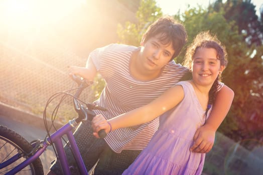 Happy young kid’s couple outdoors at sunset with bicycle