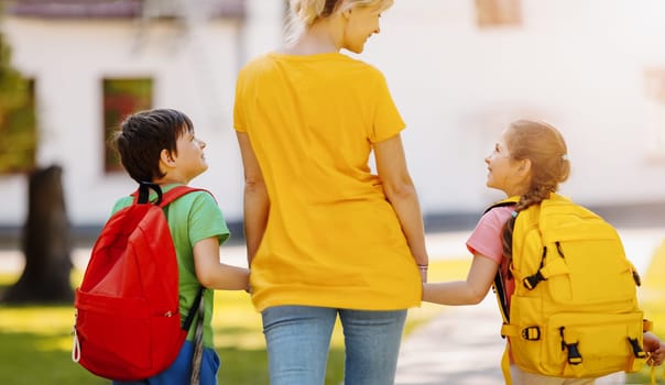 Mother walking with son and daughter on the schoolyard. Mom accompanies children to the school. Concept of family relationships and studying.