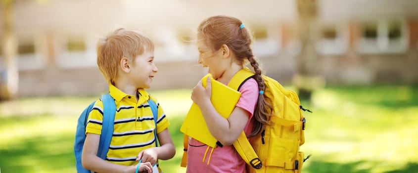 Two cute children standing in the schoolyard park. Concept of the communication between pupils and friendship.