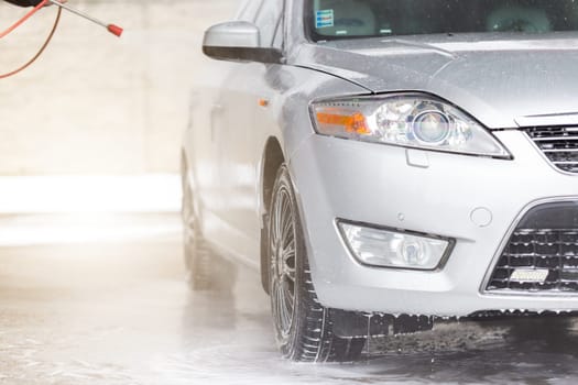 High pressure cleaning car in exterior washbasin. Touchless washing automobile with water and soap in carwash. Vehicle purifying using clearing equipment.