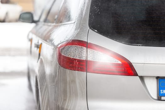 Detail of taillight of a silver modern car inside carwash with soap dripping. Close-up of a vehicle from behind after cleaning with water.