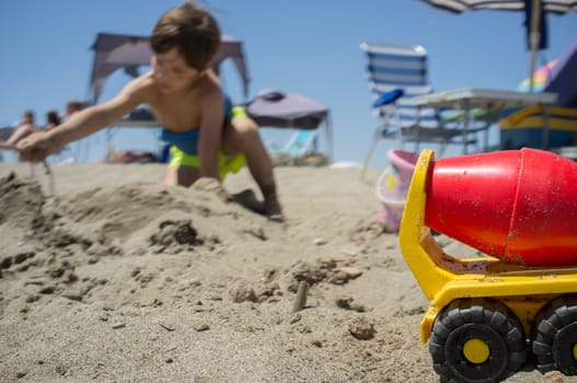 Little boy playing with sand and beach toys. Beach site full of beach furniture