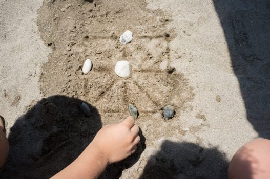 Children playing tic-tac-toe with natural board made with sand marks and beach pebbles. Overhead view