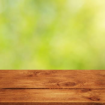 Background with blurred green leaves and empty wooden planks in the foreground. For product demonstrations, free space, layout, mockup, perspective board, background board.