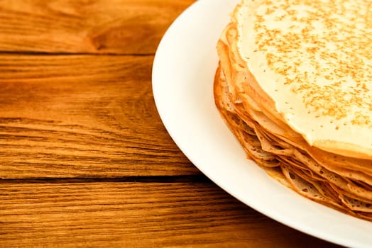 Pancakes on a plate on a wooden table. A large stack of fresh pancakes. Delicious healthy fresh pancakes. Place for advertising, logo, lettering, layout, mockup.