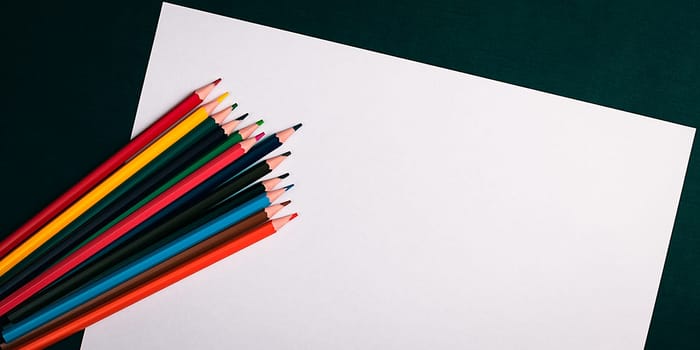 A blank white sheet and colored pencils for drawing on a plain textured background with space for copying and lettering. Layout, mockup free space.