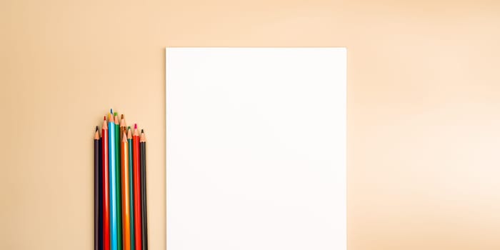 A blank white sheet and colored pencils for drawing on a plain textured background with space for copying and lettering. Layout, mockup free space.