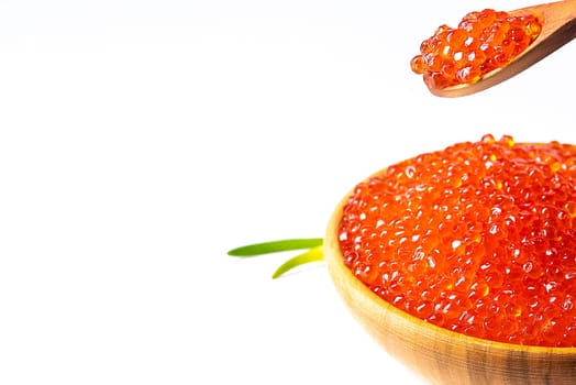 Red caviar in a wooden cup on a white background with a spoon and green onions. A large pile of bright caviar. Fresh delicious caviar. Isolated. A place for advertising, logo, label, layout, mockup. Layout, template.