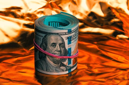 A roll of one hundred American dollars in close-up on a gold background. A big pile of cash dollars. One hundred dollar bills. Close-up, free space for captions and text.