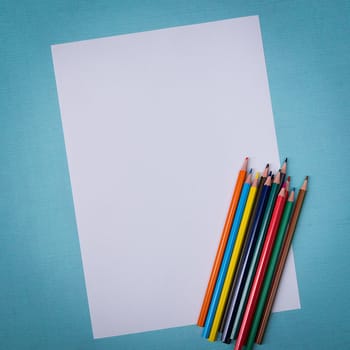 A blank white sheet and colored pencils for drawing on a plain textured background with space for copying and lettering. Layout, mockup free space.