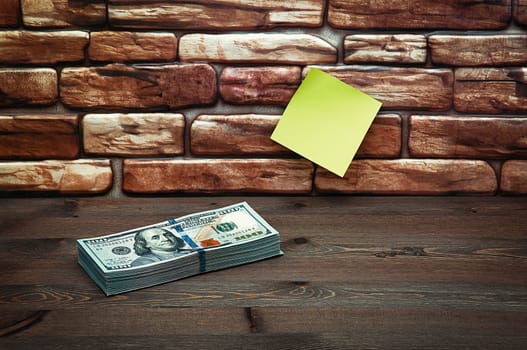 Dollars in one-hundred-dollar bills are stacked on a table near the brick wall. Dollars in a big pile. US dollars. On the brown brick wall there is a place for an inscription, a logo. Color style. Layout, template, mockup.