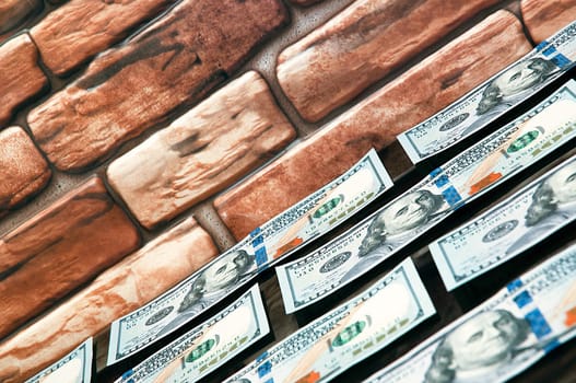 Dollars in one-hundred-dollar bills are spread out on a table near the brick wall. The dollars are arranged in a row. US dollars. On the brown brick wall there is a place for an inscription, a logo. Color style. Layout, template, mockup.