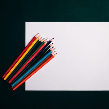 A blank white sheet and colored pencils for drawing on a plain textured background with space for copying and lettering. Layout, mockup free space.
