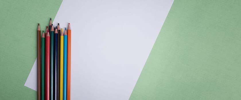 A blank white sheet and colored pencils for drawing on a plain textured background with space for copying and lettering. Layout, mockup free space.