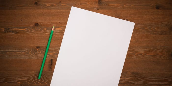 A blank white sheet and pencil for drawing on a wooden background with space for copying and lettering. Layout, mockup free space.
