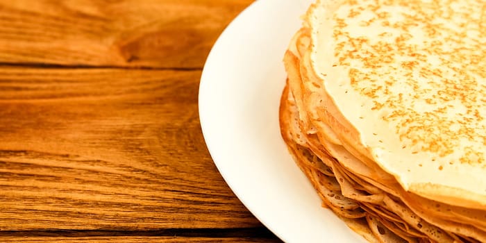 Pancakes on a plate on a wooden table. A large stack of fresh pancakes. Delicious healthy fresh pancakes. Place for advertising, logo, lettering, layout, mockup.